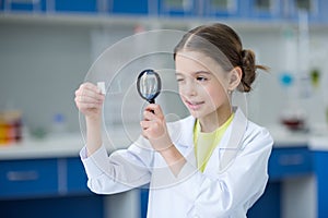Girl scientist looking at glass microscope slide through magnifier