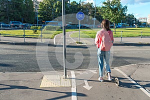 Girl on scooter summer in city. Stands with his back, crossroads, waiting for car to pass. Free space copy of text