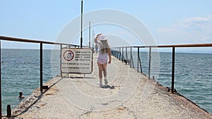 A girl on a sea breakwater approaches a warning sign and points to it