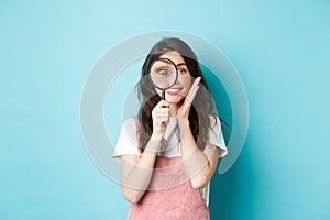 Girl searching for you. Cute smiling woman recruiter look through magnifying glass, staring at camera, investigating