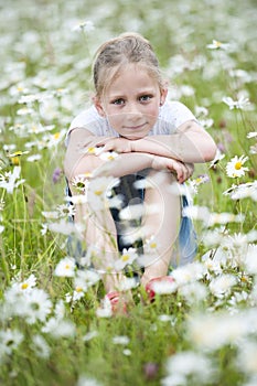 Girl seated in meadow between daisies