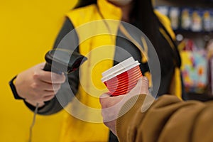 girl seller holds a barcode scanner in her hands and is counting on a man with a glass of coffee in his hand