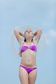 Girl in separate swimsuit posing with arms raised against sky