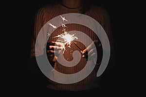 Girl sets fire to sparkler, dark background