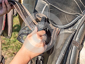 Girl setting plastic stirrups on back of leather saddle