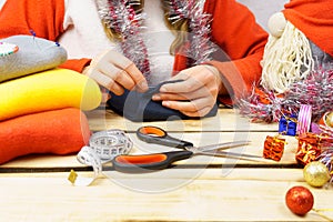 The girl sews a Christmas gnome. A girl of 30-35 years old wearing a santa claus hat makes a toy with her own hands