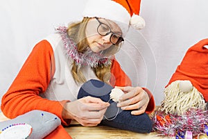 The girl sews a Christmas gnome. A girl of 30-35 years old wearing a santa claus hat makes a toy with her own hands