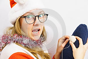 The girl sews a New Year`s gnome. Stumbled upon a needle. A 30-35 year old girl in glasses and a Santa Claus hat with an open