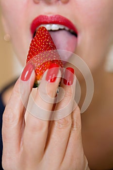 The girl sexually licks the strawberry berry with her tongue.