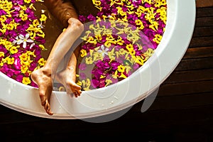 Girl shaving her leg with razor in bathroom many petals of tropical flowers.aromatherapy removal of unwanted hairs on