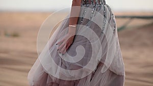 A girl in a shiny dress walks barefoot on the sand