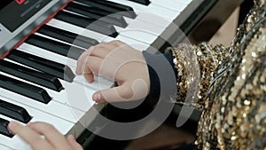A girl in a shiny golden blouse plays the piano. Fingers of the child press white keys of an electronic synthesizer