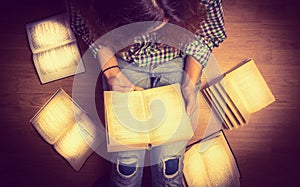 Girl in a shirt holding a book sitting on the floor around her spread open books close up retro toning photo
