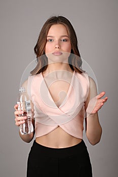 Girl in shirt posing with bottle of water. Close up. Gray background