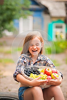 Girl in shirt and shorts with a basket of fruit. Girl farmer with apples and grapes. Concept of ecological food, person