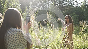 The girl shoots her friend using her phone in the forest in a beautiful sunny background light. The girlfriend is spinning,