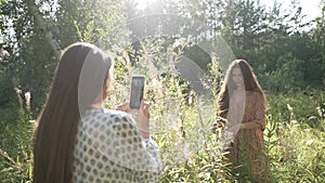A girl shoots a video of her friend using her phone in the forest in a beautiful sunny background light. The girlfriend is