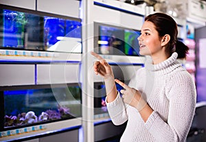 Girl in shop looking at different aquariums with colorful fish on several rows of shelves with aquariums