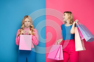 Girl with shopping bags looking at offended sister on pink and blue background