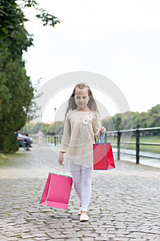 Girl shopping on calm face carries bags, urban background. Kid girl with long hair fond of shopping. Fashionista girl