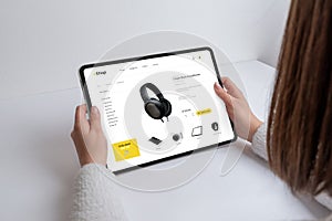 Girl shops online for headphones, gadgets, and devices on a modern e-commerce webpage using a tablet