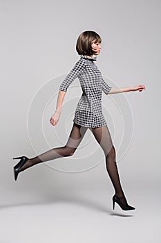 Girl in a short dress, black tights and shoes jumps in the studio on a white background