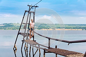 Girl with a short haircut stands on a rustic water intake against the backdrop of a river in the sun