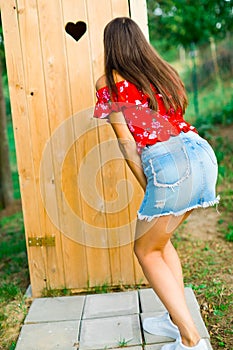 A girl in short jeans skirt waiting for wooden toiled