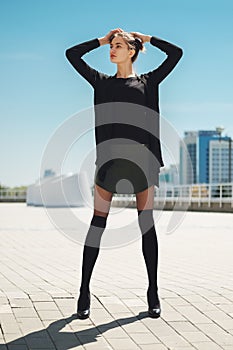 Girl in short leather skirt and legs with knee socks on top of tights enjoys the sun with hands behind the head