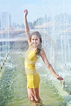 Girl in a short slinky dress with long wet hair and legs in water droplets in the city fountain