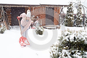 A girl with a shovel cleans the snow in the village.