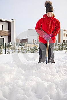 Girl shoveling snow on home drive way. Beautiful snowy garden or front yard. Teenager removing snow with a shovel in the