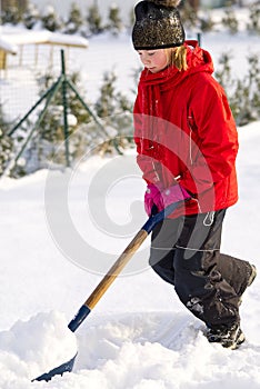 Girl shoveling snow on home drive way. Beautiful snowy garden or front yard. Teenager removing snow with a shovel in the