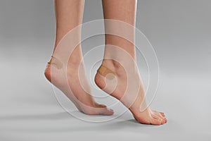 Girl showing feet with sticking plasters on grey background, closeup