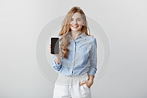 Girl showing new phone to colleague. Portrait of charming friendly-looking european fashion blogger in formal blue