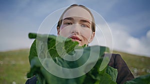 Girl showing organic vegetable closeup. Woman with braids standing green field
