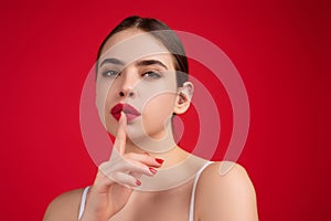 Girl showing shhh sign with finger near lips, standing over studio background. Women emotions. Secret young woman saying