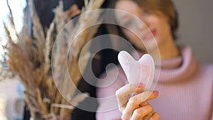 The girl shows a massage gua sha massager made from natural stone rose quartz that is used to stimulate lymphatic system