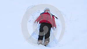 Girl shows snow angel on white snow in winter. Child is playing with snow. Christmas Holidays