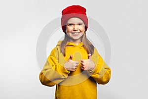 Girl shows thumb up, agrees with something, like gesture, wears yellow hoodie