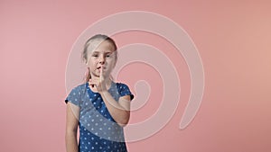 A girl shows a tizo gesture, a finger near her lips. Blue dress with polka dots.