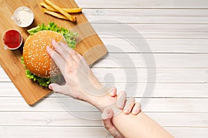 The girl shows willpower by holding with her left hand, her right hand that reaches for a hamburger. Diet and healthy nutrition,