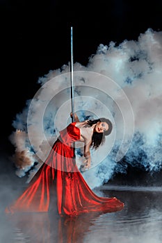 Girl shrouded in smoke dancing around a pole dance.