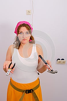 The girl shrugs - problems with the repair in the house. Hammer and pliers in the hands of a confused woman