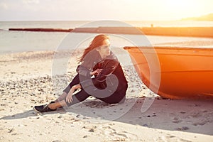 A girl sideways near a red boat on the beach by the sea
