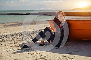 A girl sideways near a red boat on the beach by the sea