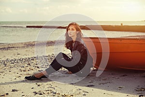 A girl sideways near a red boat on the beach by the sea