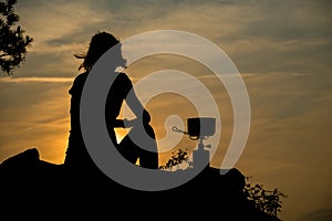 Girl silhouette cooking coffee on camping stove at sunrise light, outdoor picnic camping