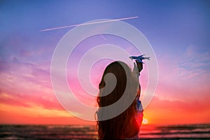 Girl silhouette holding airplane model in her hand in front of scenic sunset sky background. air transportation concept.