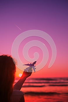 Girl silhouette holding airplane model in her hand in front of scenic sunset sky background. air transportation concept.